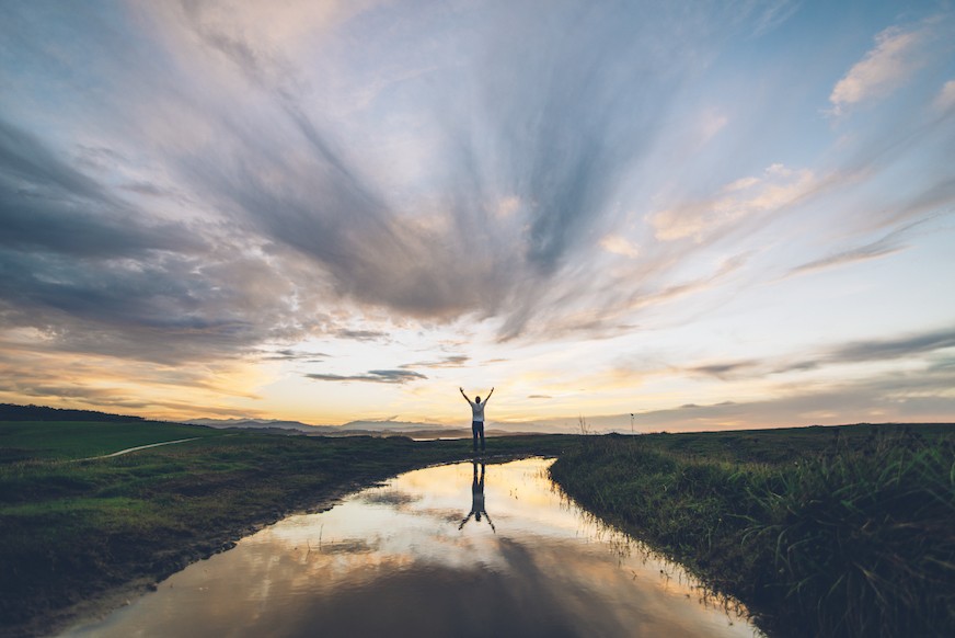 Man standing in marshland raising his hands to the sky