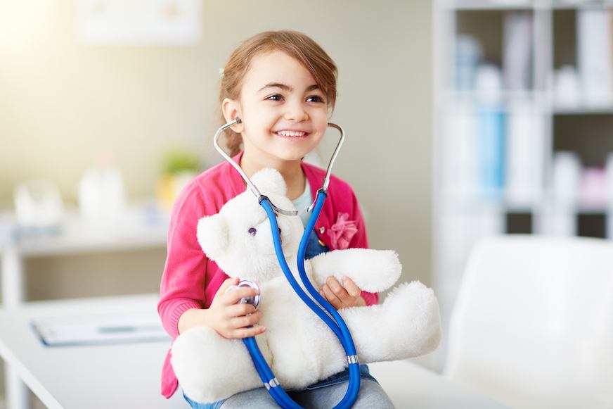 Little girl using a stethoscope on her toy bear