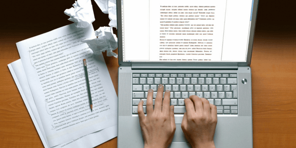 Hands Typing on a Laptop Keyboard Next to Papers